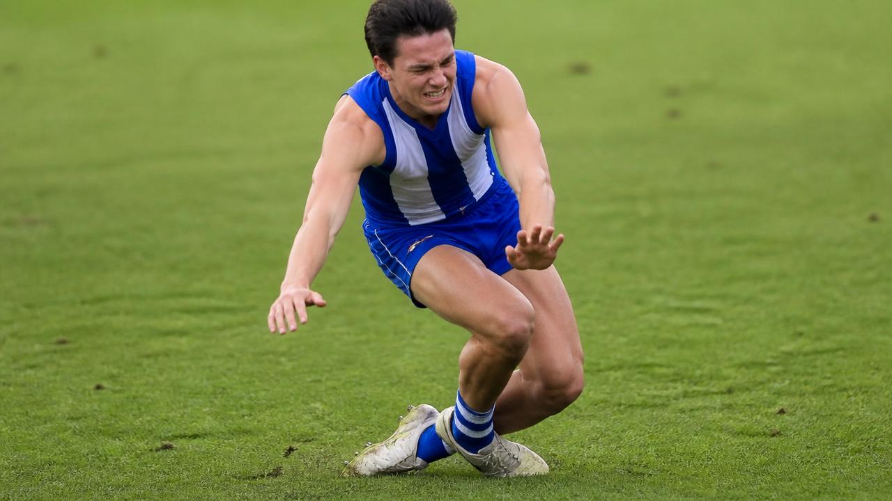 A footballer on the pitch holding their knee in pain immediately after a non-contact twisting injury.