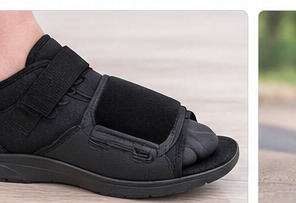 A black post-operative surgical shoe worn on the foot.