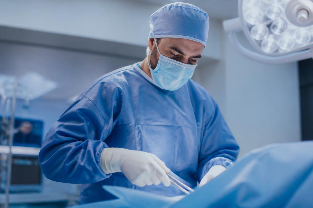 A surgeon in blue scrubs performing an operation in a modern operating theatre.