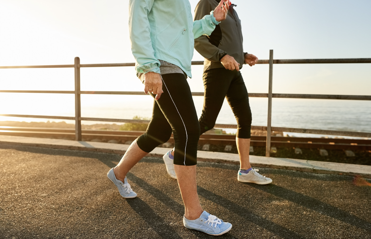 Two people walking briskly along a coastal path at sunset.